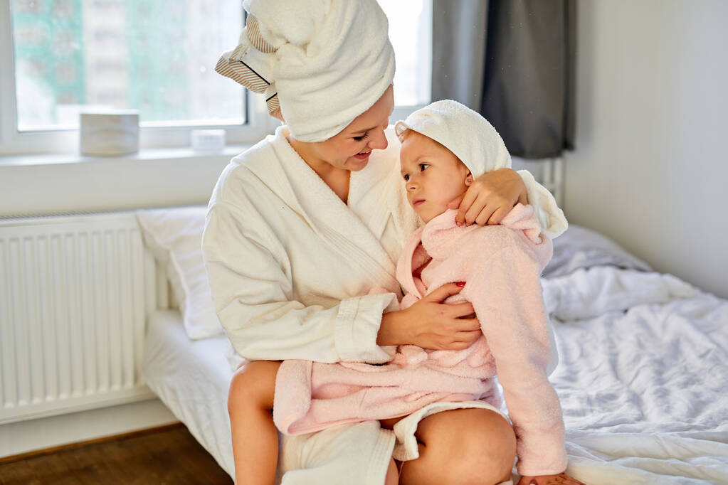 όμορφη γυναίκα με μπουρνούζι και πετσέτα να απολαύσετε το χρόνο στο κρεβάτι με την κόρη κοριτσάκι - Φωτογραφία, εικόνα