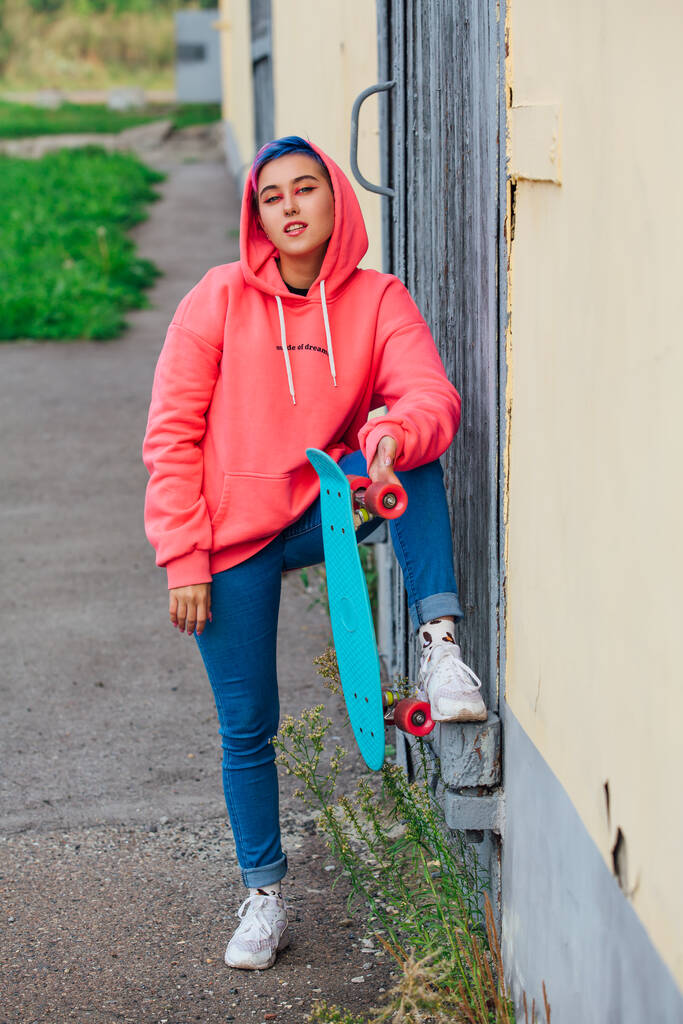 Jeune femme élégante avec des cheveux courts de couleur tenant skateboard en plastique bleu à la main. Concept jeunesse. - Photo, image