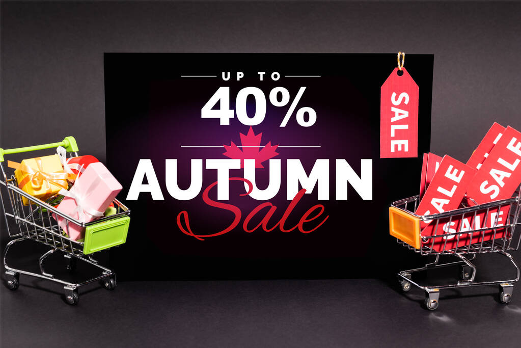small presents in toy shopping carts near placard with up to 40 percent, autumn sale lettering and sale tag on dark background - Photo, Image