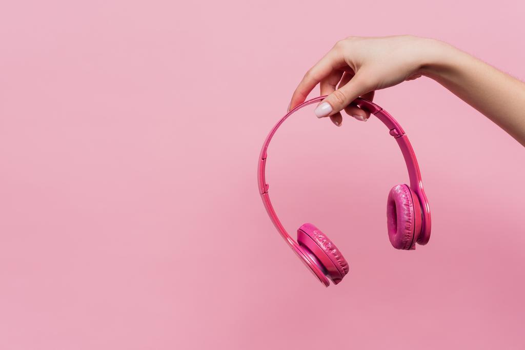 μερική άποψη της γυναίκας που κρατά ασύρματα ακουστικά στο χέρι απομονώνονται σε ροζ - Φωτογραφία, εικόνα