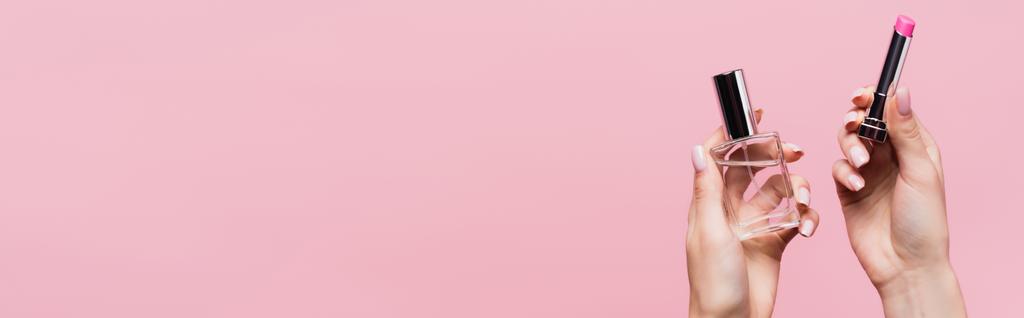 vista ritagliata di donna che tiene rossetto e bottiglia con profumo isolato su rosa, banner - Foto, immagini
