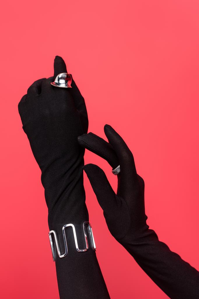 καλλιεργημένη άποψη των γυναικείων χεριών σε μαύρα γάντια με δαχτυλίδια και βραχιόλι που απομονώνονται σε κόκκινο - Φωτογραφία, εικόνα