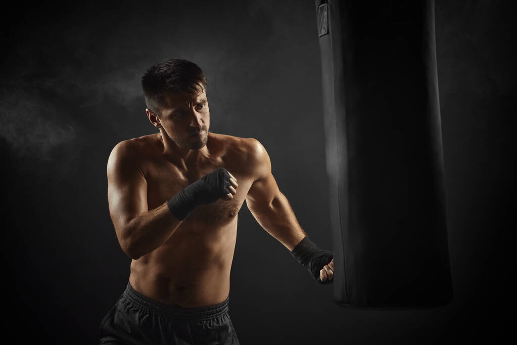 boxeador en boxeo negro envuelve perforación en bolsa de boxeo - Foto, Imagen