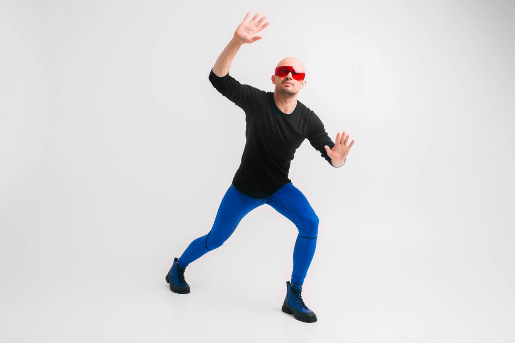 Fashion portrait of stylish man in blue tights and indigo boots stretching and exercising over white studio background. - Photo, Image