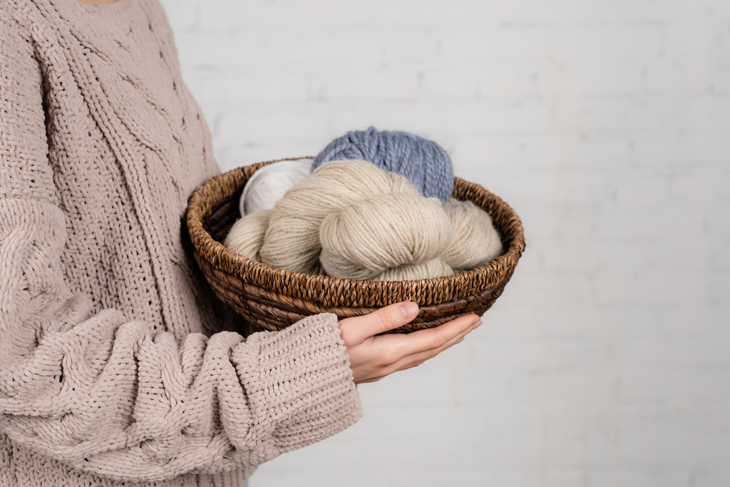 Vista recortada de la mujer en suéter de punto con cesta de sujeción con hilo de lana sobre fondo blanco - Foto, imagen