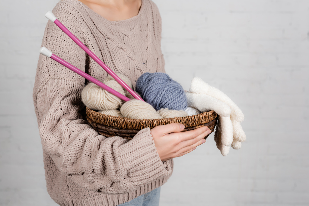 白い背景に編み物の針、糸、手袋を持つ若い女性のトリミングビュー - 写真・画像