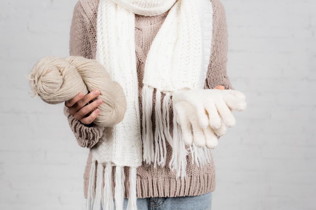 Cropped view of woman in sweater and scarf holding yarn and gloves on white background - Photo, Image