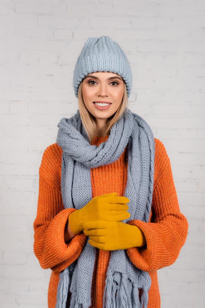 Jonge vrouw met warme hoed, gebreide trui en handschoenen kijkend naar camera op witte achtergrond - Foto, afbeelding