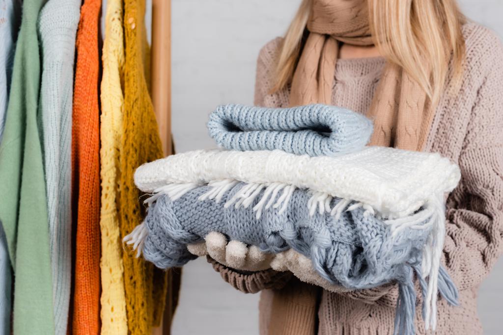 Cropped view of woman holding knitwear near hanger rack with sweaters on white background - Photo, Image