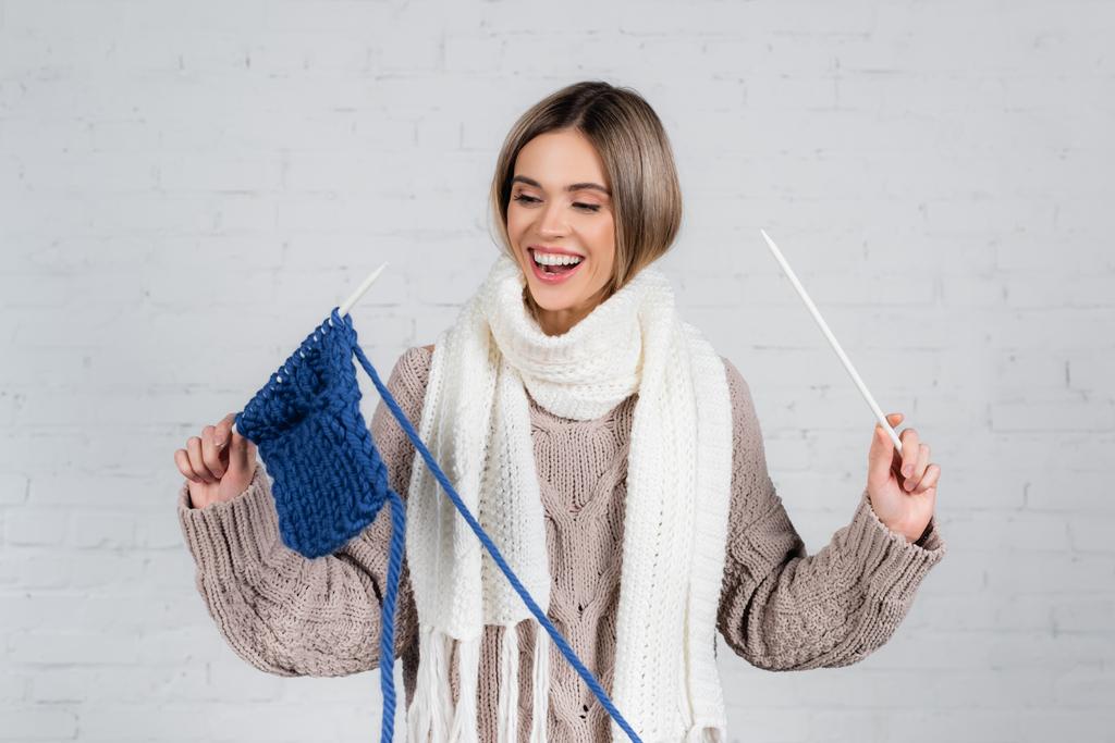 正の女性でスカーフとセーター保持糸と編み物針近くの白いレンガの壁に - 写真・画像