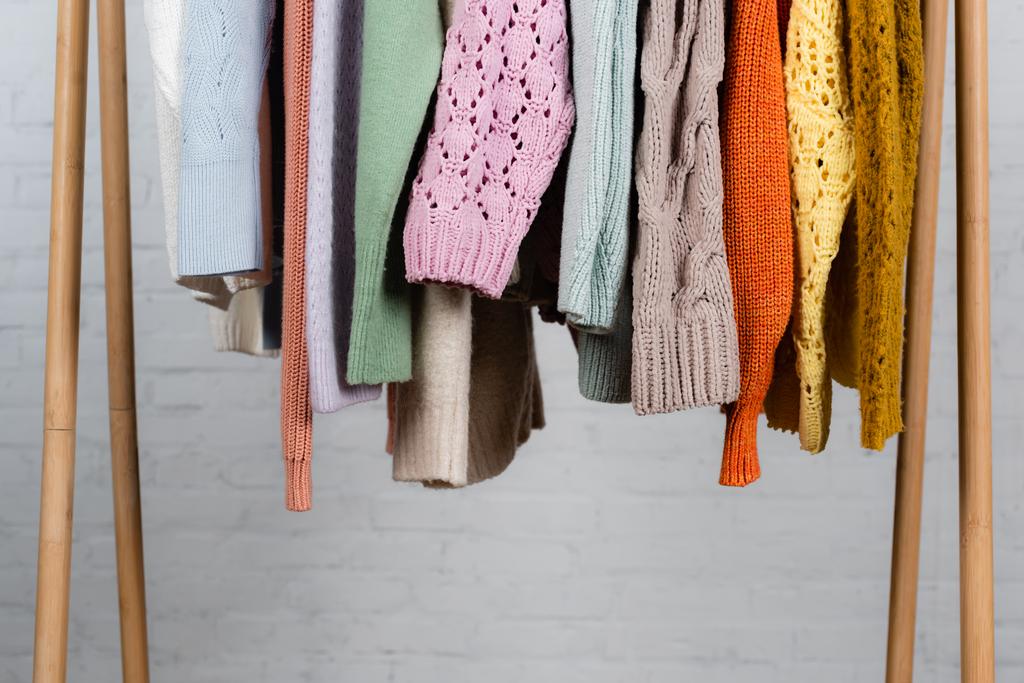Knitted sweaters on wooden hanger rack on white background - Photo, Image