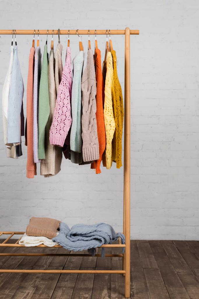 Wooden hanger rack with colorful knitted sweaters near white brick wall - Photo, Image