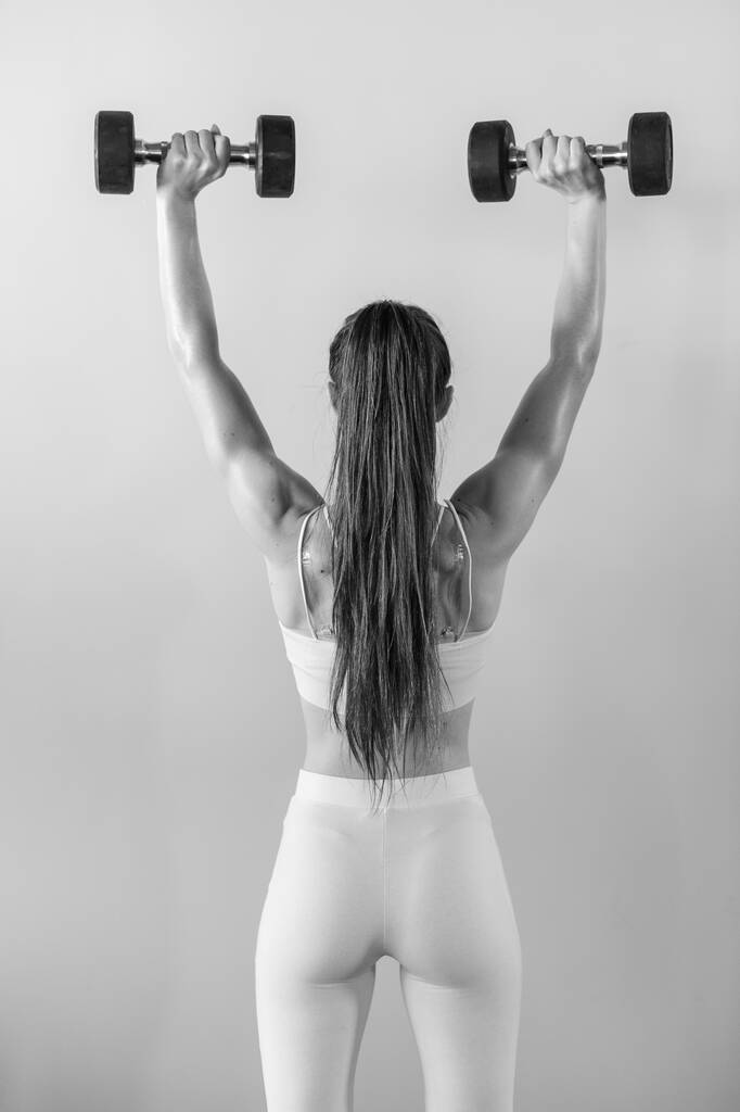 Athletische Bodybuilderin mit Hanteln. Hübsches brünettes Mädchen mit Muskeln, die Gewichte heben  - Foto, Bild