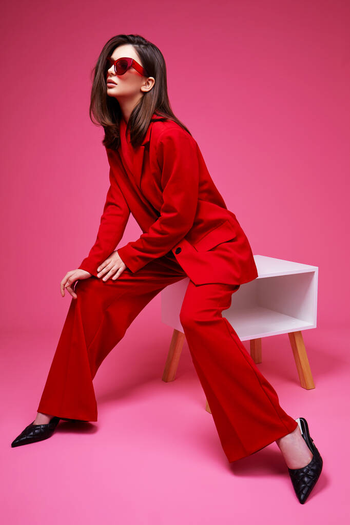 Μοντέλα μόδας σε κόκκινο κοστούμι και γυαλιά ηλίου. Φωτογραφία στούντιο. - Φωτογραφία, εικόνα