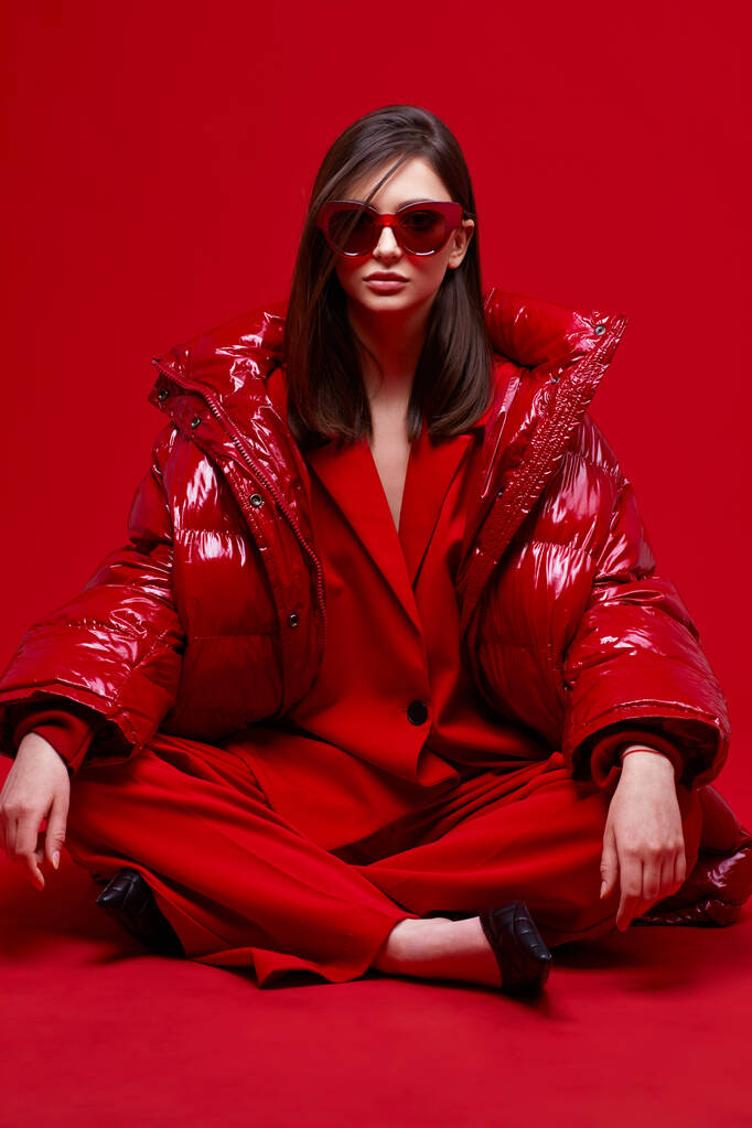 Modelka w czerwonym garniturze, kurtce i okularach przeciwsłonecznych. Zdjęcia studyjne. - Zdjęcie, obraz