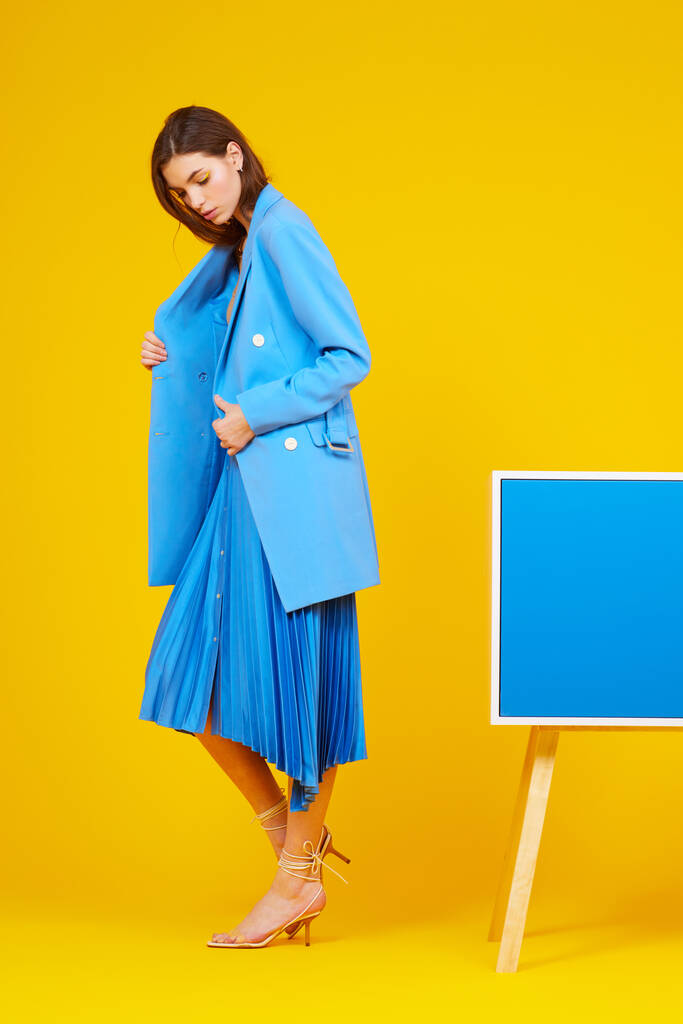 Retrato de alta moda de mujer joven y elegante en chaqueta azul y falda. Fondo amarillo, plano de estudio - Foto, Imagen