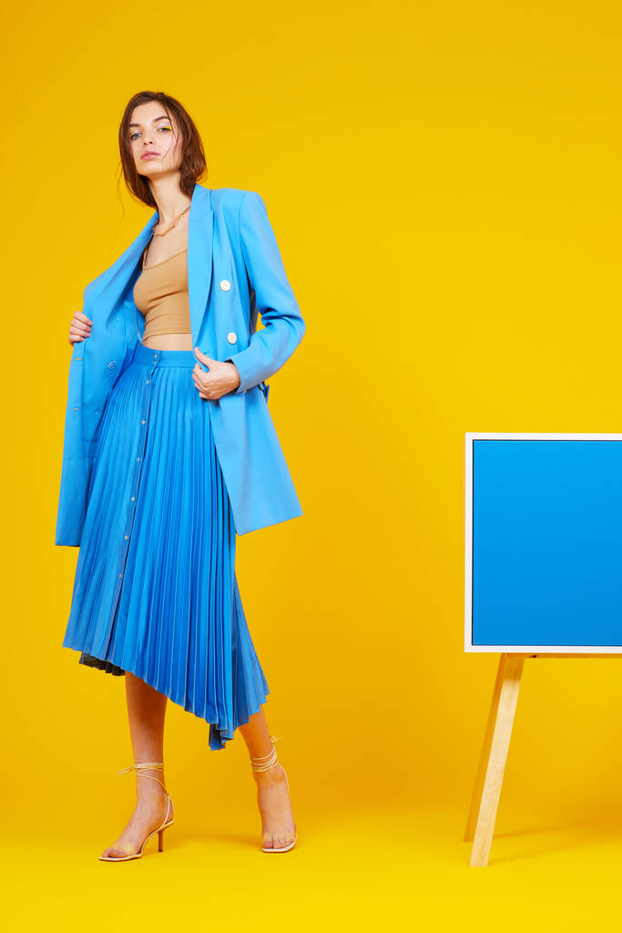 Portrait de haute couture de jeune femme élégante en veste bleue et jupe. Fond jaune, plan studio - Photo, image