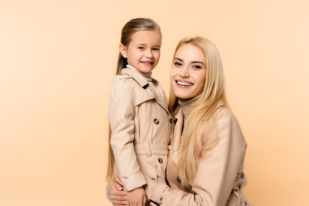 cheerful blonde mother hugging happy daughter isolated on beige - Photo, Image