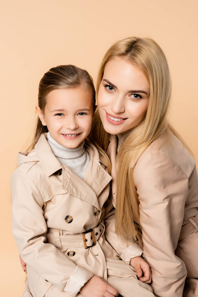 joyeuse mère blonde et fille heureuse regardant la caméra isolée sur beige - Photo, image