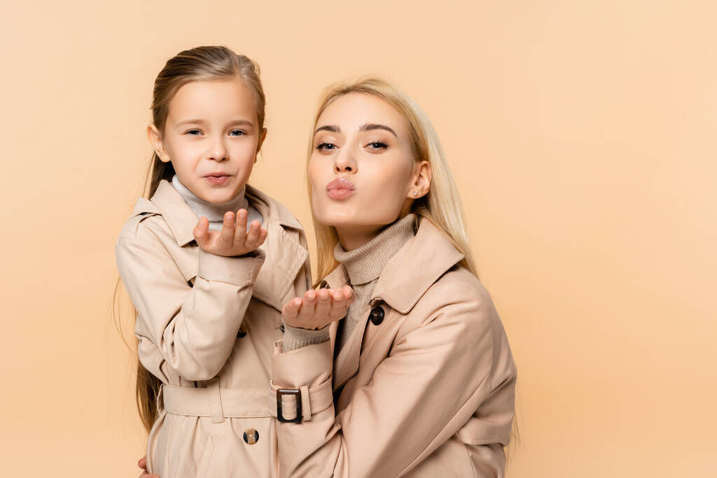 madre e figlia in cappotti inviare baci aria isolati su beige - Foto, immagini