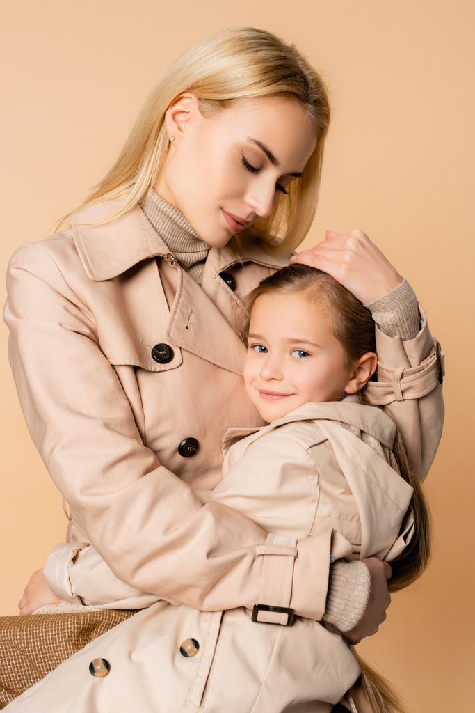 cuidado y madre rubia abrazando hija aislada en beige - Foto, Imagen