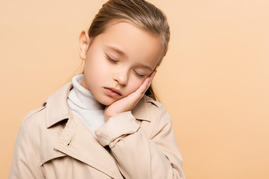 сонный ребенок с закрытыми глазами в траншеи пальто изолированы на бежевый - Фото, изображение