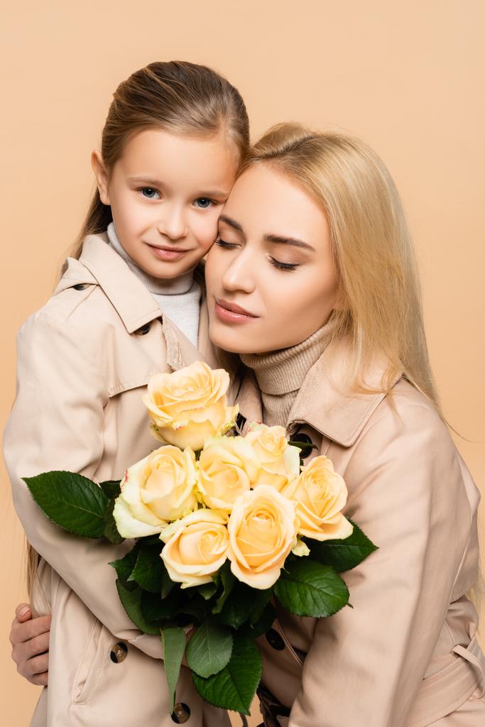 mère tenant des fleurs et embrassant fille isolé sur beige - Photo, image