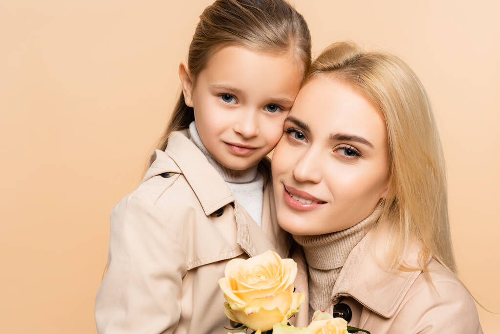 joyful mother holding flowers and hugging daughter isolated on beige - Photo, Image