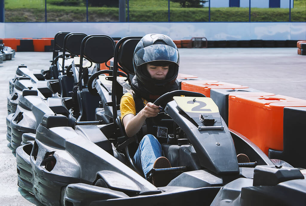 Kasklı genç bir kız açık hava go-kart 'ıyla spor bir arabaya biniyor. Karting motor sporlarında popüler bir eğlence biçimidir.. - Fotoğraf, Görsel
