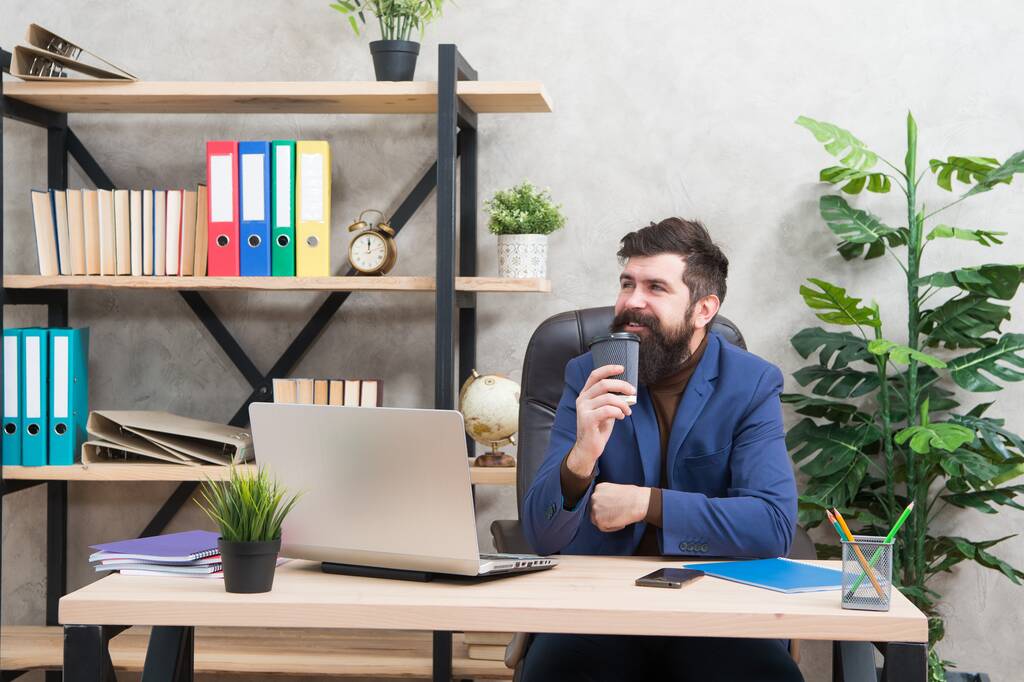 Happy hipster in formele kleding drinken koffie bij managers bureaublad in moderne werkkamer, kantoor - Foto, afbeelding