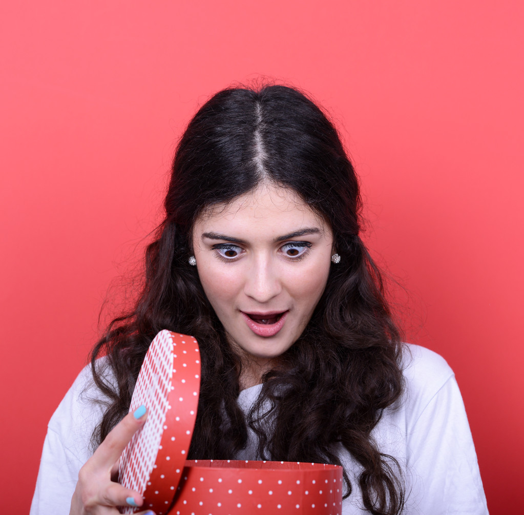 Retrato de mujer feliz abriendo caja de regalo sobre fondo rojo - Foto, imagen