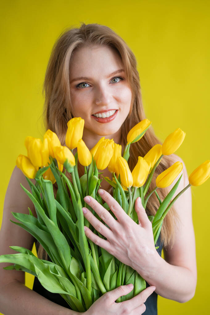 黄色の背景に黄色のチューリップの軍隊を持つ白人女性。国際女性デー。春の花の花束 - 写真・画像