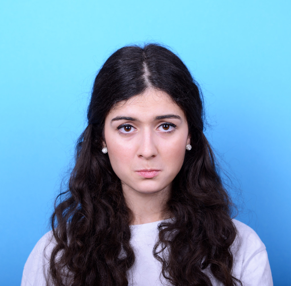 Portret van triest meisje tegen blauwe achtergrond - Foto, afbeelding