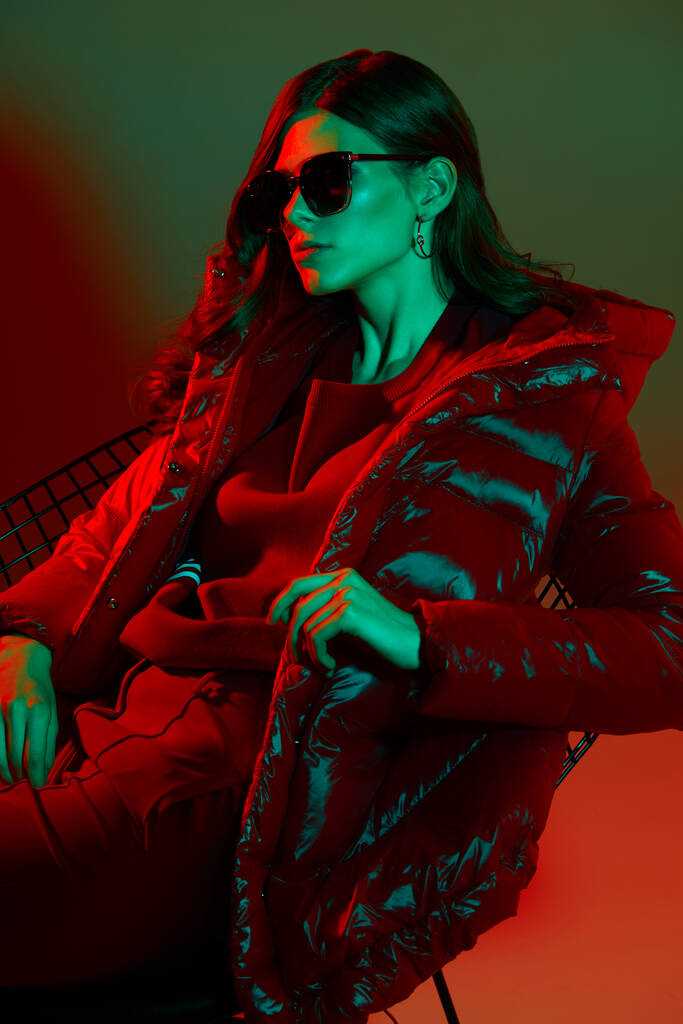 Retrato de moda de mujer elegante de moda en chaqueta roja. Luz de neón, gafas de sol, toma de estudio - Foto, Imagen