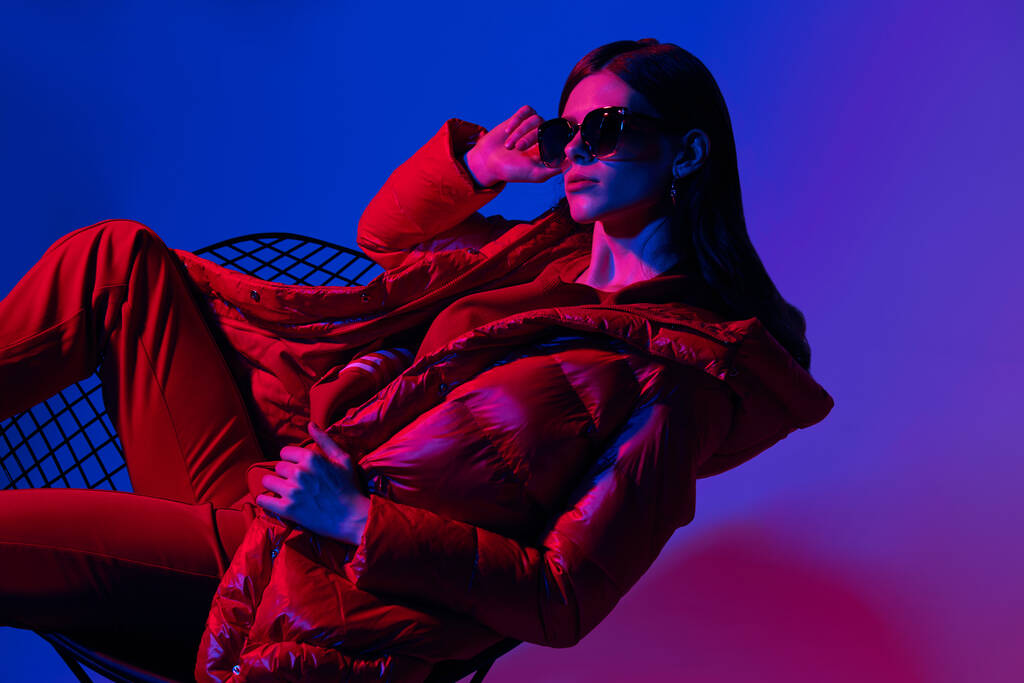 Divat portré elegáns divatos nő piros le kabát. Neon fény, napszemüveg, stúdiófelvétel - Fotó, kép