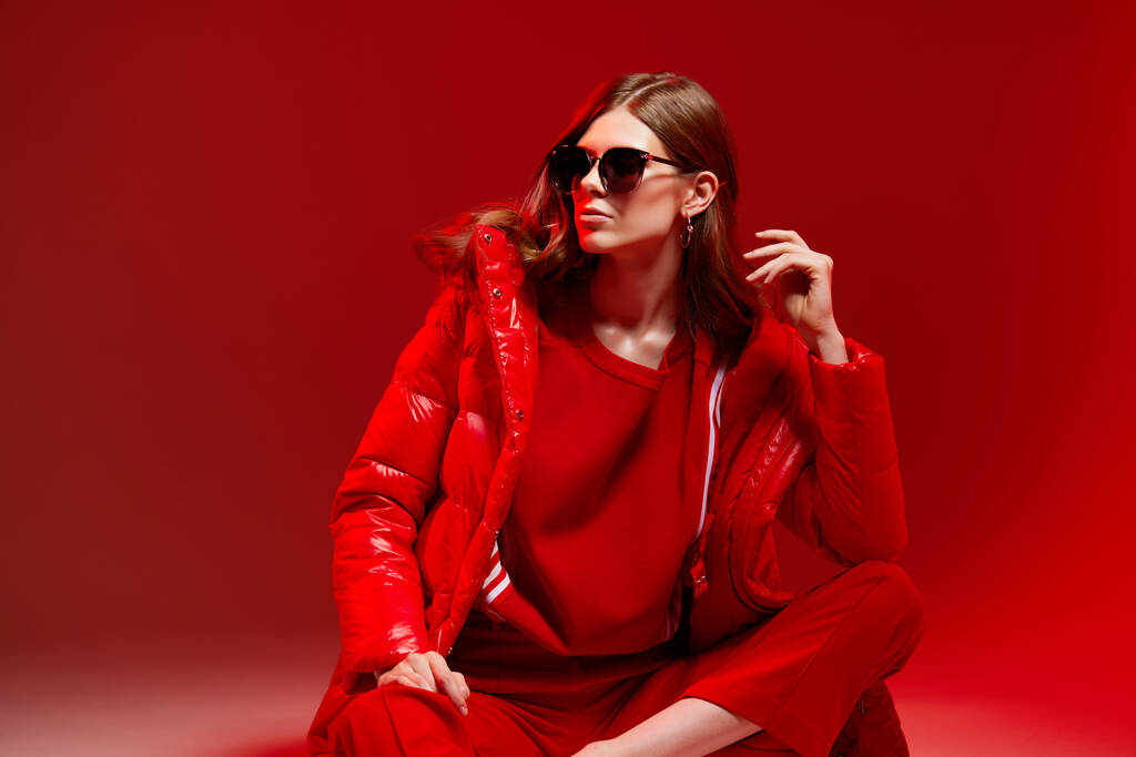 Fashion portret van elegante trendy vrouw in rood donsjas. Neon licht, zonnebril, studio opname - Foto, afbeelding