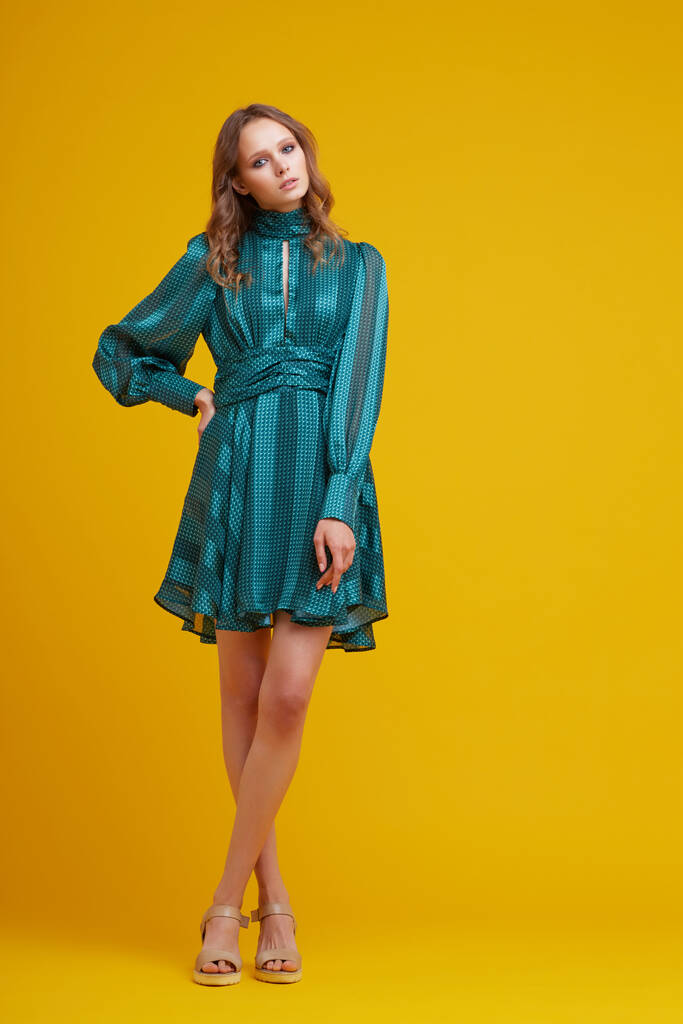 Yeşil elbiseli güzel bir genç kadın. Sarı arka plan, moda stüdyosu. - Fotoğraf, Görsel