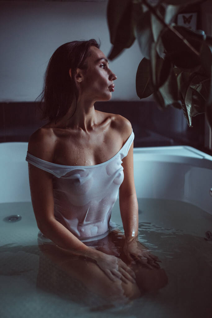 Une jeune belle fille, en T-shirt blanc et lin fin dans une salle de bain, dans un jacuzzi, elle porte un brûleur humide sur son corps, nue - Photo, image