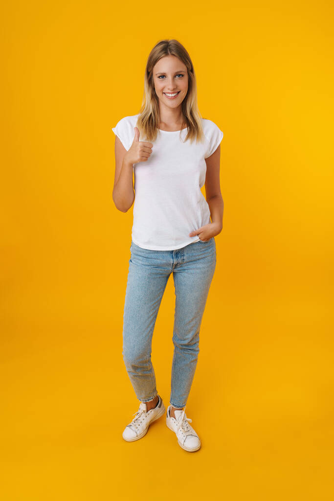 Cheerful beautiful girl smiling and showing thumb up isolated over yellow background - Photo, Image