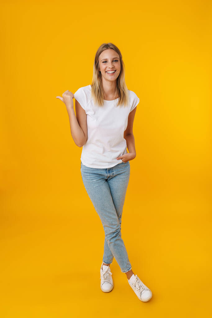 Cheerful beautiful girl smiling while pointing finger aside isolated over yellow background - Photo, Image