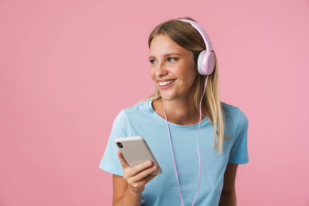 Портрет счастливой женщины, слушающей музыку в наушниках на розовом фоне - Фото, изображение