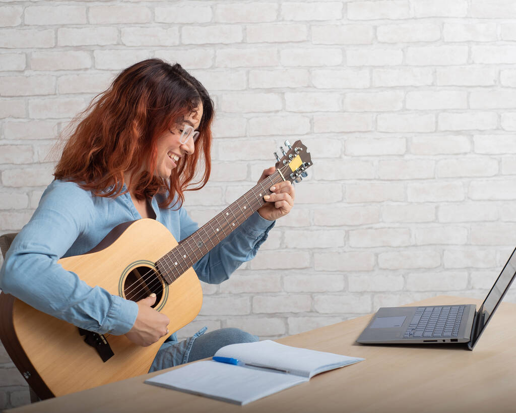 La donna caucasica insegna a suonare la chitarra da remoto sul portatile. Formazione musicale online - Foto, immagini