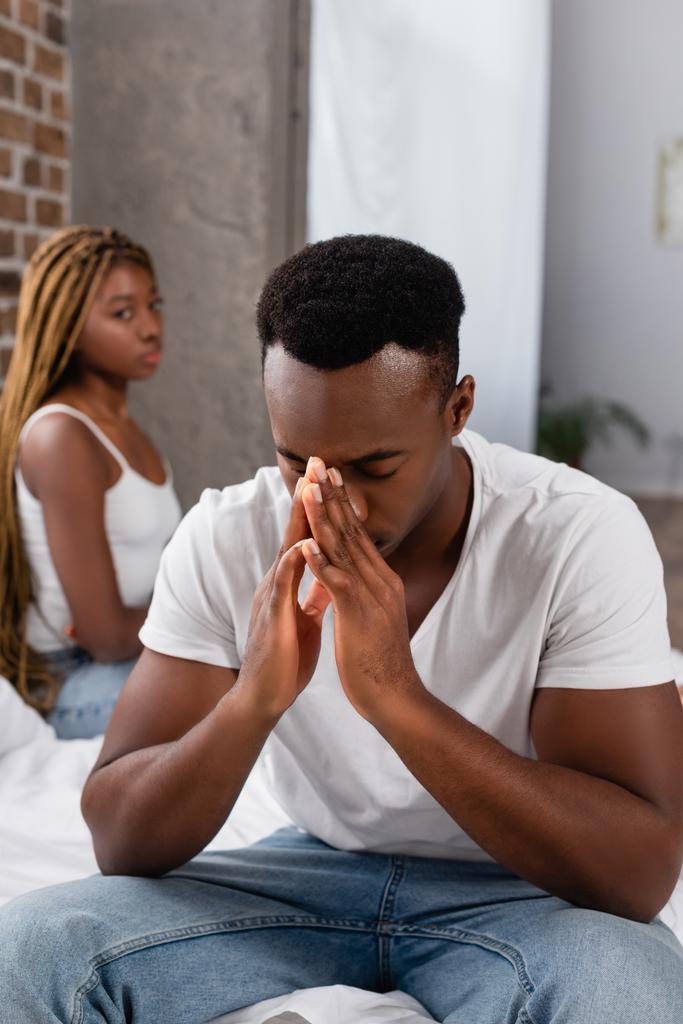 Homme afro-américain déprimé assis près de la petite amie sur fond flou dans la chambre  - Photo, image
