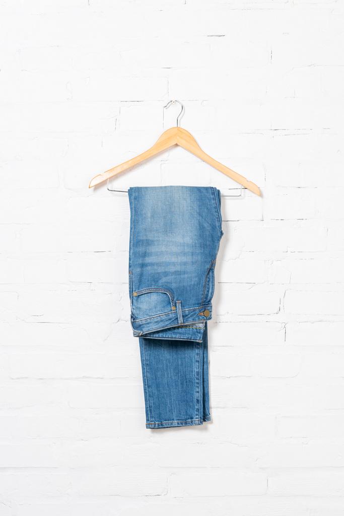 hanger with blue jeans near white brick wall - Photo, Image