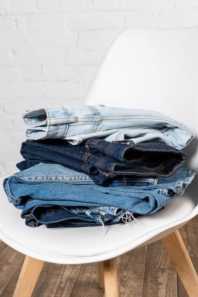 стек різних джинсових одягу на білому стільці біля цегляної стіни
 - Фото, зображення