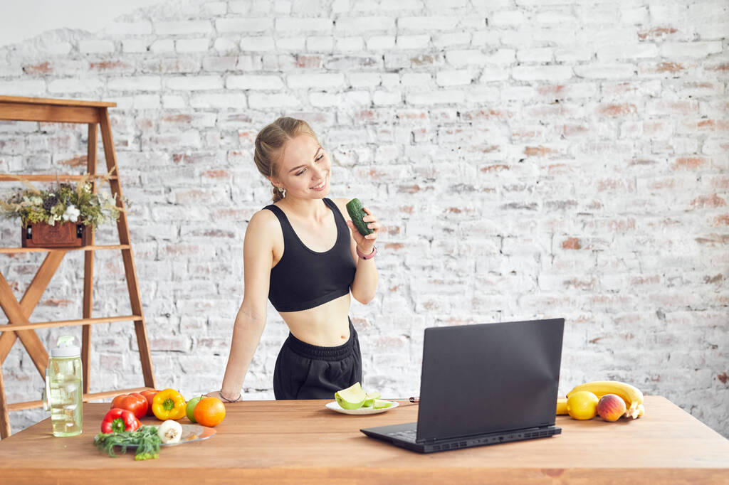 Kaunis nuori nainen yllään urheilullinen vaatteet kannettavan tietokoneen avulla, etsivät yksinkertaisia reseptejä kotona. - Valokuva, kuva