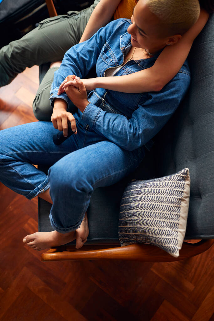 Αγαπώντας το ίδιο φύλο θηλυκό ζευγάρι κρατώντας τα χέρια ξαπλωμένος στον καναπέ στο σπίτι βλέποντας τηλεόραση και χαλαρώνοντας μαζί - Φωτογραφία, εικόνα