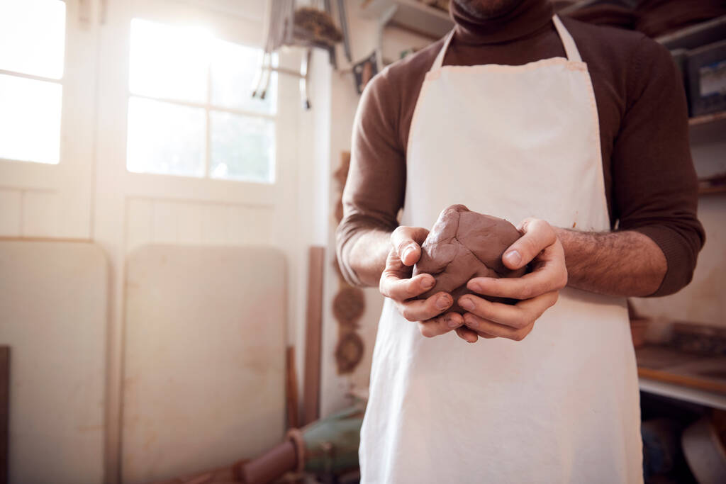 Close-up van de mannelijke pottenbakker dragen van een pron Holding Lump Of Clay In Keramiek Studio - Foto, afbeelding