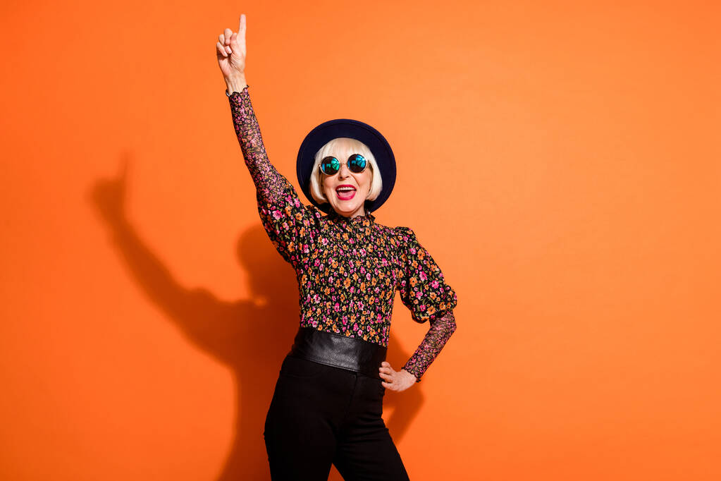 Photo of cheerful smiling crazy happy positive old woman dance point finger copyspace isolated on orange color background - Photo, Image