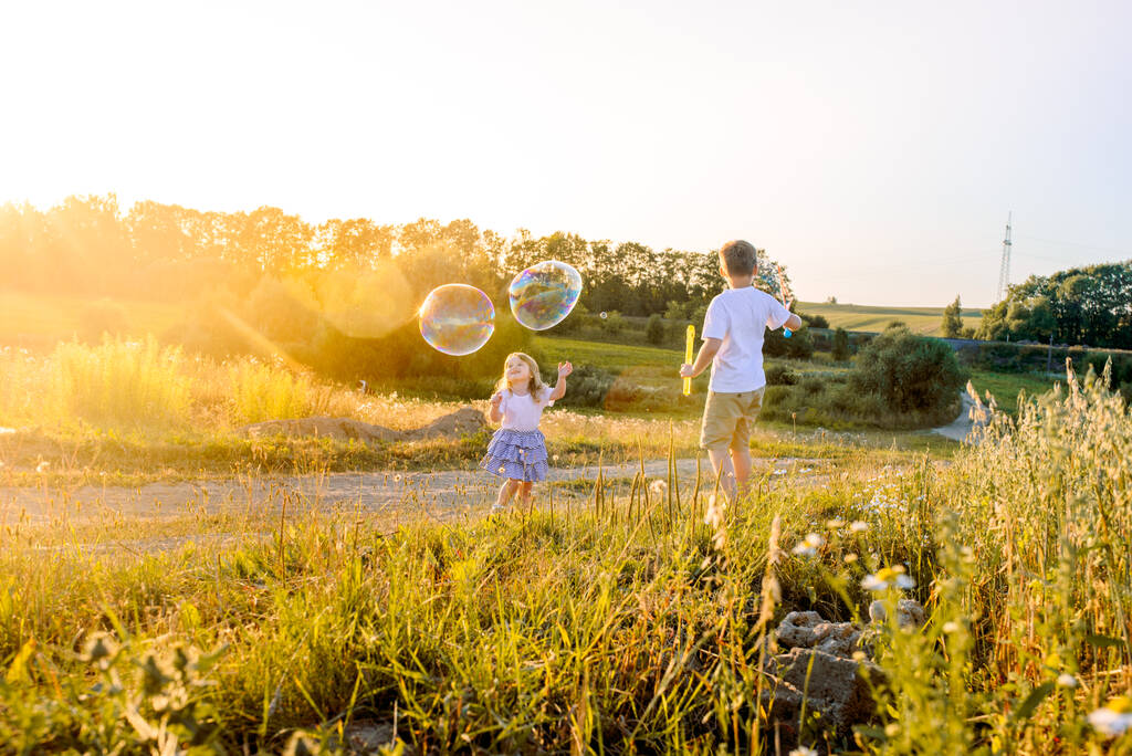 Boldog gyerekek játszanak szappanbuborékokkal a nyári természetben. Buborékok a naplementében - Fotó, kép
